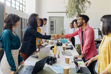 Businessman and businesswoman shaking hands amidst colleagues at workplace - MEUF06780