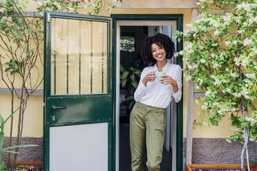 Lächelnde junge Geschäftsfrau beim Kaffee am Eingang - MEUF06788