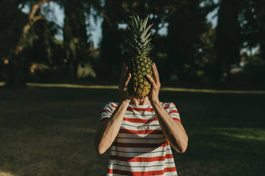 Frau bedeckt Gesicht mit Ananas im Park - DMGF00760