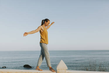 Frau balanciert auf dem Geländer am Meer an einem sonnigen Tag - DMGF00763