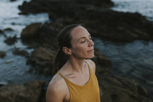 Frau mit geschlossenen Augen stehend am Meeresufer bei Sonnenuntergang - DMGF00767