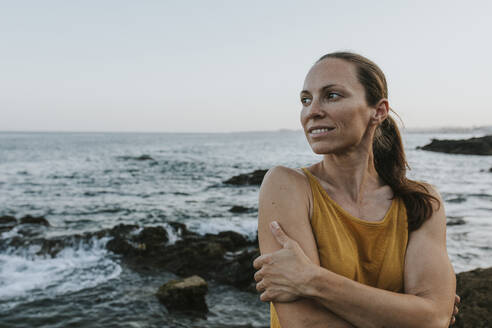 Happy woman hugging self at sea shore on sunset - DMGF00771