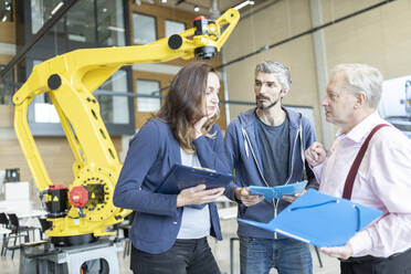 Engineers in factory having meeting in front of industrial robot - WESTF24831