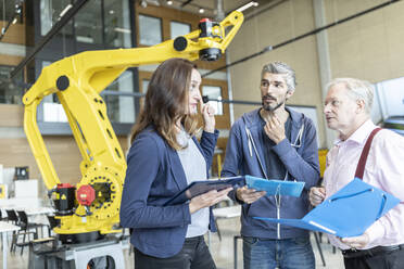 Engineers in factory having meeting in front of industrial robot - WESTF24833