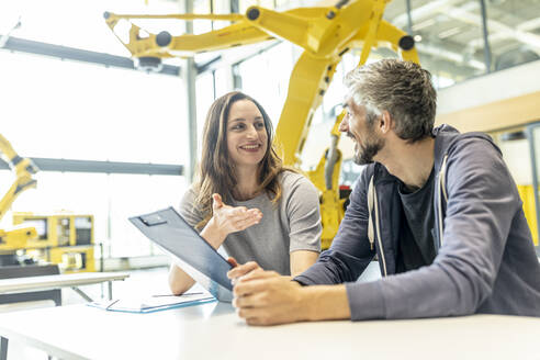 Technician and engineer sitting in factory discussing work solutions - WESTF24866