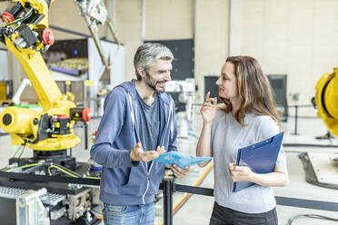 Colleagues discussing technical report in front of industrial robot - WESTF24869