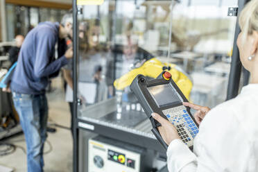 Frau in Fabrik mit Steuerung von Industrieroboter - WESTF24877