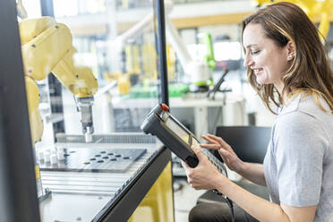 Frau in Fabrik mit Steuerung von Industrieroboter - WESTF24885