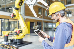 Skilled worker controlling robot arm with digital tablet - WESTF24898