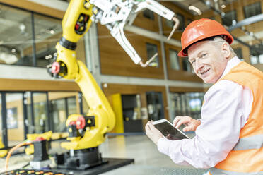 Selbstbewusster Facharbeiter steuert Roboterarm mit digitalem Tablet - WESTF24900