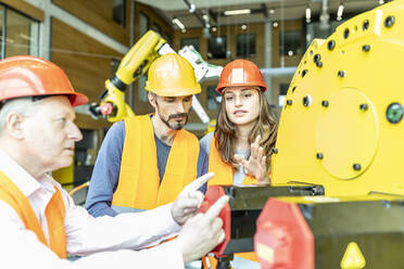 Male and female colleagues discussing robotic machine in industrial factory - WESTF24910