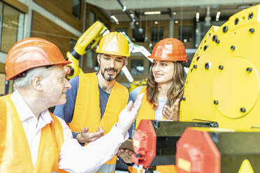 Männliche und weibliche Kollegen diskutieren über eine Robotermaschine in einer industriellen Fabrik - WESTF24911