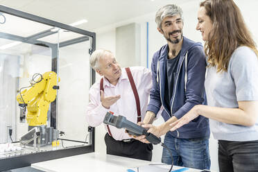 Colleagues watching woman programming robot arm with digital control - WESTF24933
