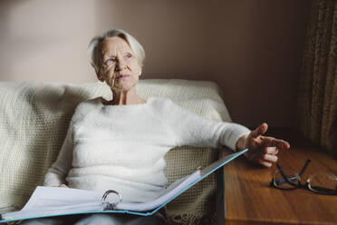 Senior woman with documents sitting on sofa at home - OSF00200