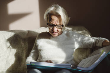 Senior woman with short white hair reading documents at home - OSF00203