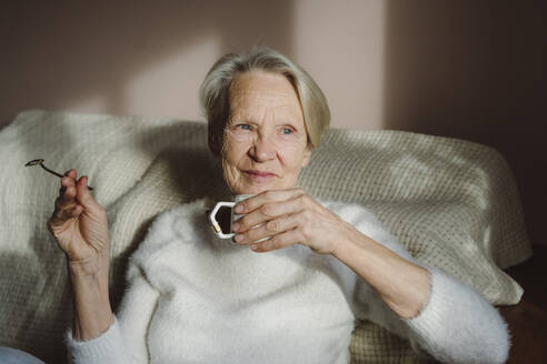Glückliche ältere Frau mit Kaffeetasse, die zu Hause sitzt - OSF00207