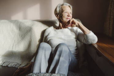 Smiling senior woman with hand on chin sitting at home - OSF00209