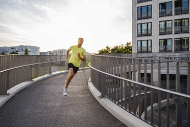 Young man jogging on elevated walkway in city - DIGF18195