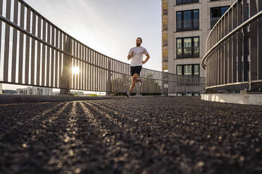 Junger Mann in Sportkleidung läuft auf einer Fußgängerbrücke - DIGF18206