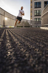 Junger Mann in Sportkleidung joggt auf einer Fußgängerbrücke - DIGF18207