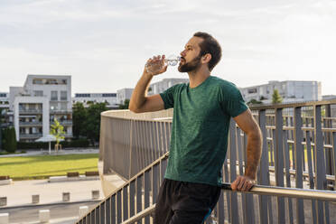Bearded man drinking water leaning on railing - DIGF18209