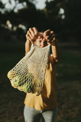 Woman holding fruits in mesh bag - DMGF00777