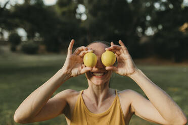 Smiling woman holding lemons in front of face - DMGF00783