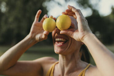 Cheerful woman covering face with lemons - DMGF00784