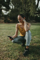 Woman using mobile phone crouching at park - DMGF00789