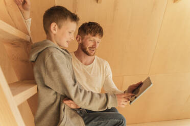 Father and son using tablet pc for creating home interior in eco wooden house - OSF00242
