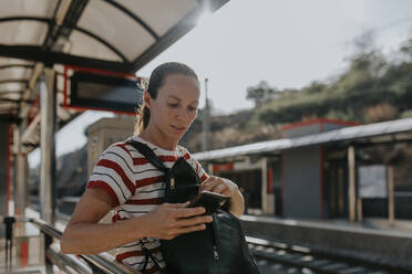 Woman using phone waiting at railroad station - DMGF00791