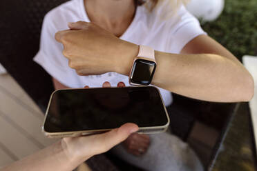 Frau beim kontaktlosen Bezahlen mit einer Smartwatch auf einem von der Kassiererin gehaltenen Mobiltelefon - SIF00216