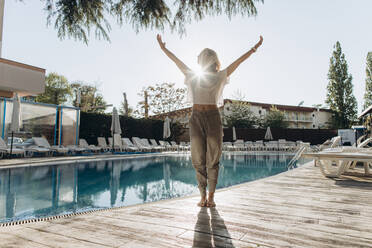 Woman with arms raised standing by swimming pool on sunny day - SIF00229