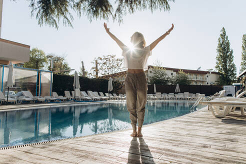 Frau mit erhobenen Armen am Schwimmbad stehend an einem sonnigen Tag - SIF00229