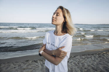 Smiling woman with arms crossed standing in front of sea - SIF00232