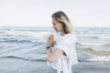 Happy woman with hands clasped standing in front of sea - SIF00237