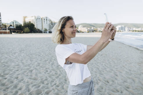 Lächelnde Frau nimmt Selfie durch Smartphone am Strand - SIF00240