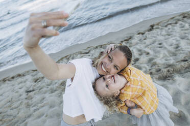 Happy mother with daughter taking selfie through smart phone at beach - SIF00243