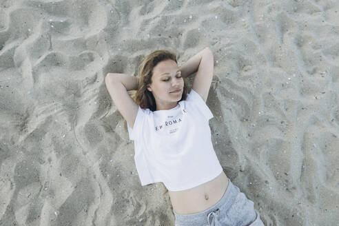 Lächelnde Frau mit Händen hinter dem Kopf am Strand liegend - SIF00247