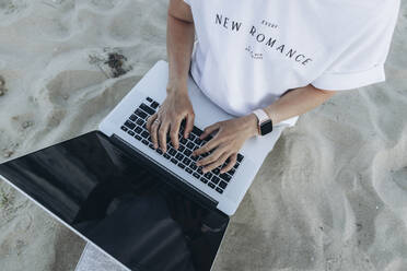 Frau mit Laptop auf Sand am Strand sitzend - SIF00250