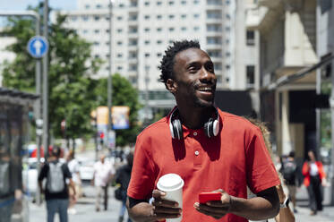 Smiling man holding mobile phone and coffee cup - PGF01131