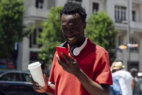 Lächelnder Mann mit Kaffeetasse und Mobiltelefon - PGF01134