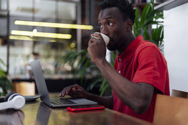 Mann trinkt Kaffee und sitzt mit Laptop im Cafe - PGF01147