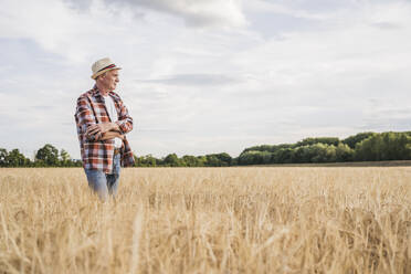 Thoughtful farmer standing with arms crossed at wheat field - UUF26681