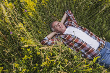 Senior farmer with eyes closed lying amidst plants - UUF26689