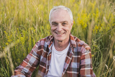 Happy farmer with white hair sitting in front of plants - UUF26694