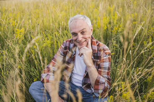 Glücklicher Landwirt sitzt inmitten von Pflanzen auf einem Feld - UUF26695