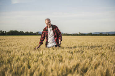 Happy farmer standing amidst wheat crops on field - UUF26708