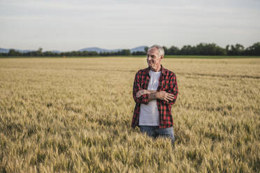 Smiling senior farmer with arms crossed standing at wheat field - UUF26710