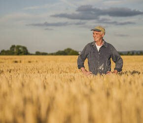 Glücklicher älterer Landwirt in einem Weizenfeld stehend - UUF26715